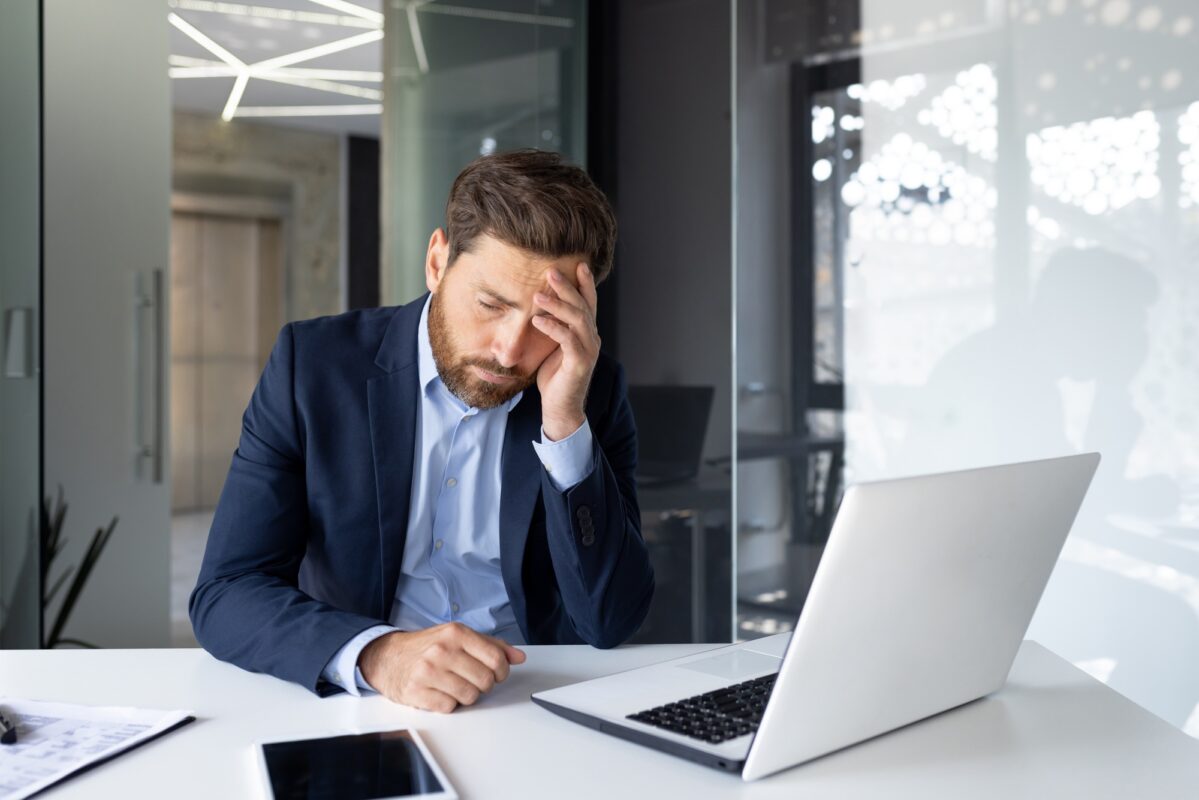 Stressed businessman with headache working late on laptop in modern office, overworked employee