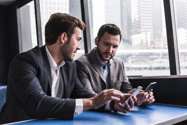 Two businessmen with cell phones talking on passenger deck of a ferry